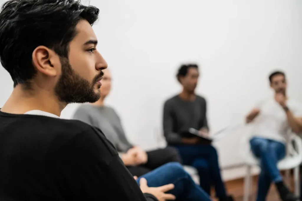 The Grove Recovery | man listens in a group setting indoors